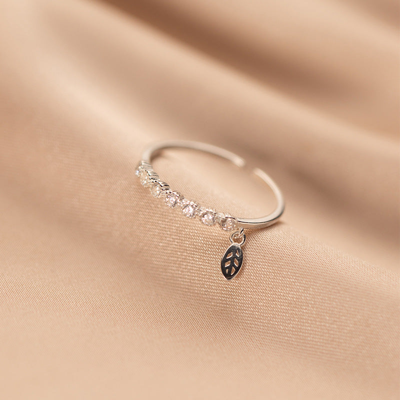 A close-up of a 925 sterling silver adjustable ring from a set of five, featuring an elegant leaf design and a sparkling dangling cubic zirconia charm.