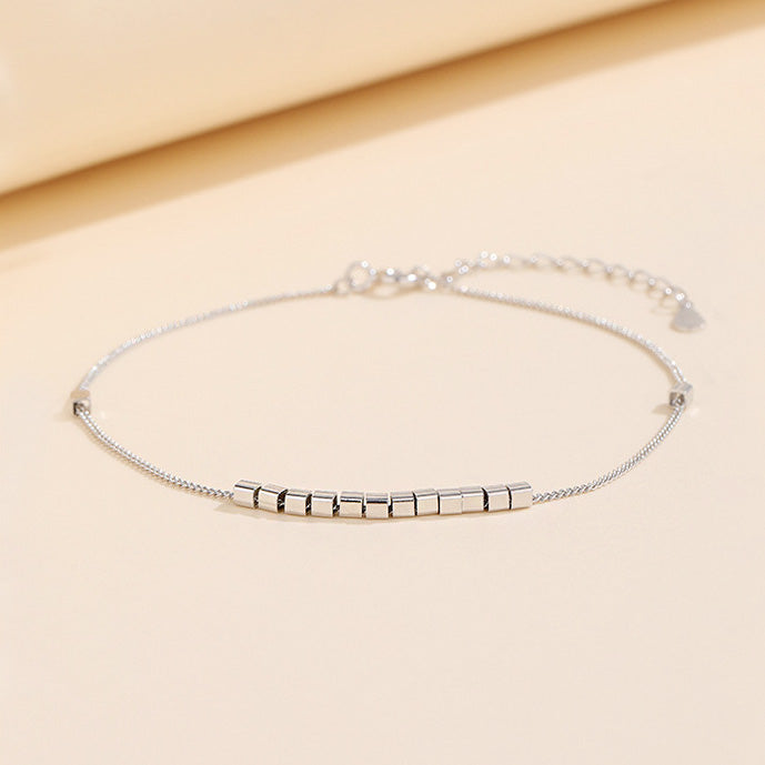 A delicate 925 sterling silver box chain bracelet featuring a central bar of square beads and an adjustable clasp with a heart charm.