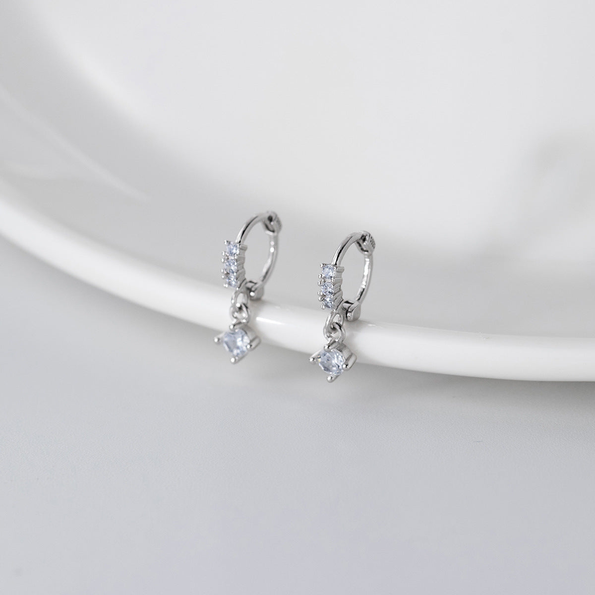 A pair of sterling silver geometric square zirconia earrings with a minimalist design, displayed on a clean white background to highlight their sparkling stones.