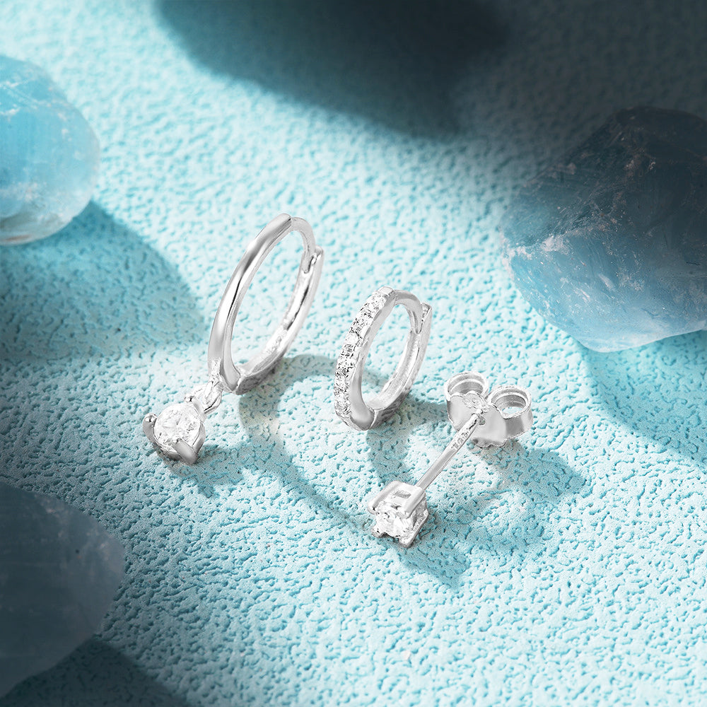 A collection of 925 sterling silver stud and hoop earrings with zircon gemstones from the 5-pair set, displayed on a light blue surface.