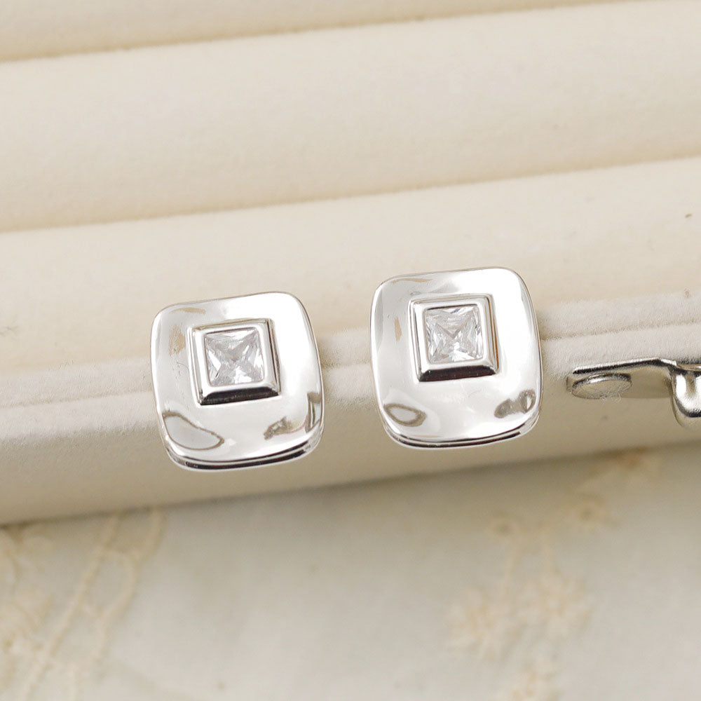 A close-up view of a pair of silver-plated square stud earrings, each featuring a sparkling cubic zirconia stone, displayed on a neutral background.