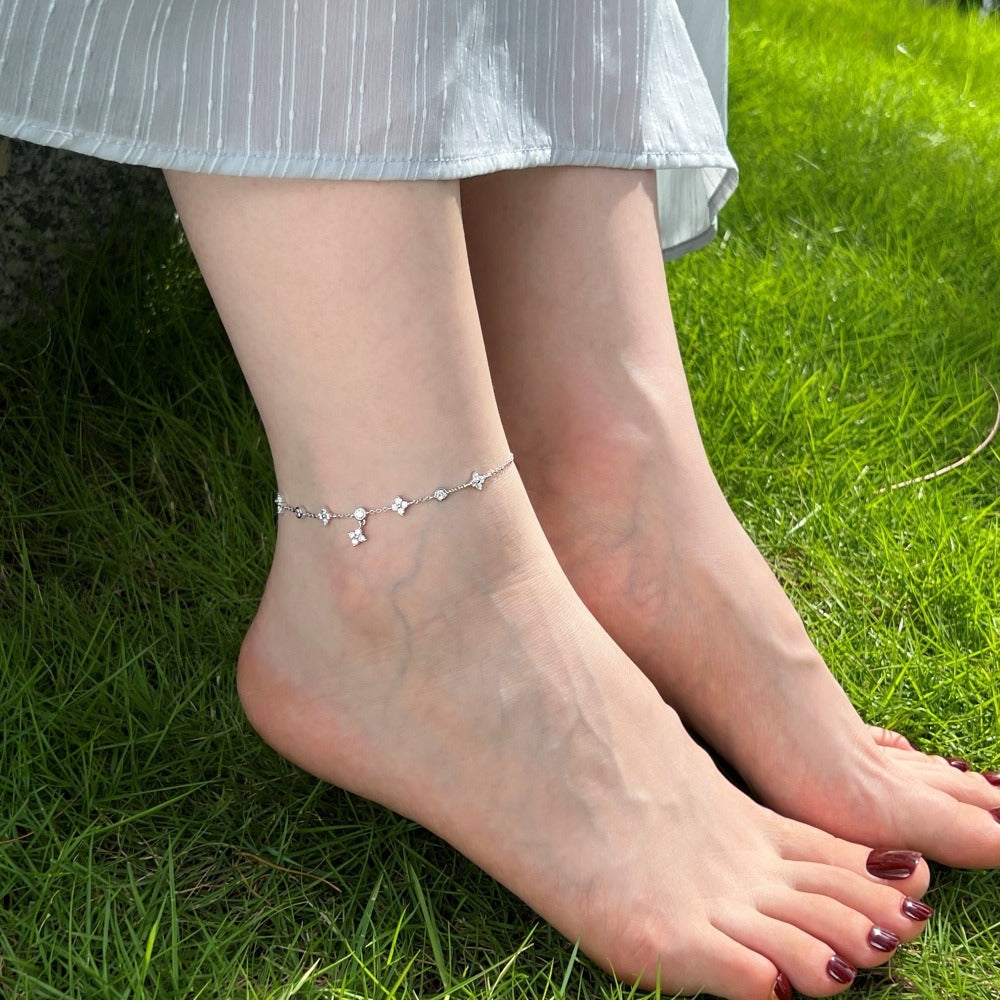 A woman's ankle adorned with a delicate 925 sterling silver anklet featuring a lucky four-leaf clover charm, perfect for beachwear.