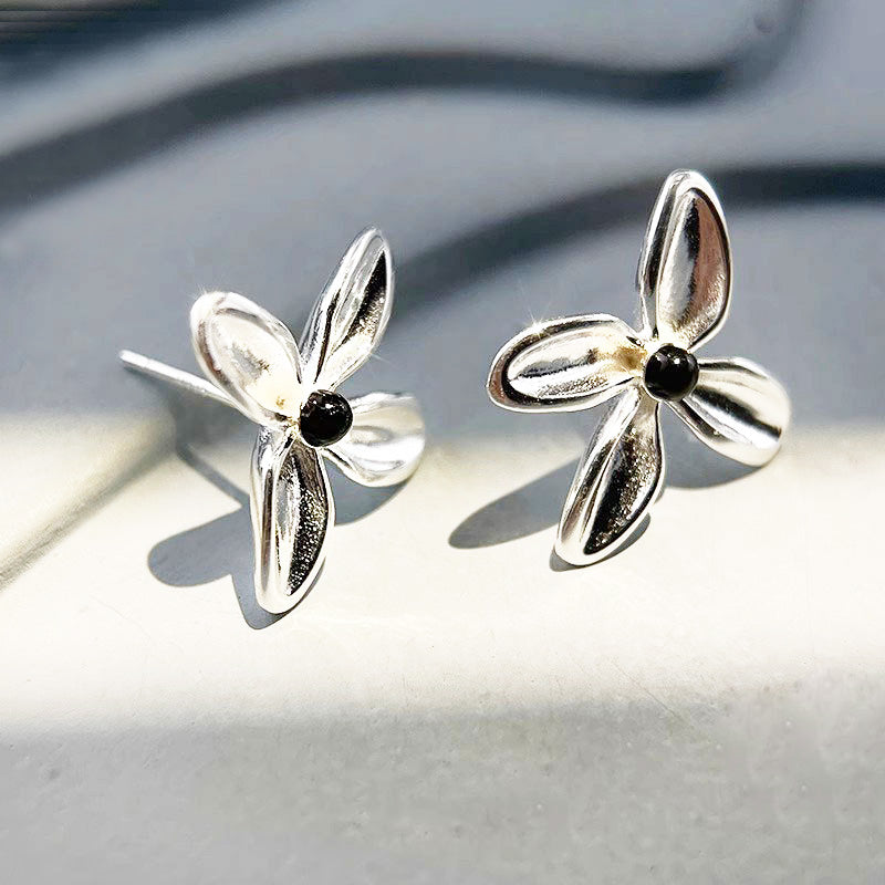 A close-up of a pair of 925 sterling silver flower stud earrings with polished black onyx centers, on a clean white background.
