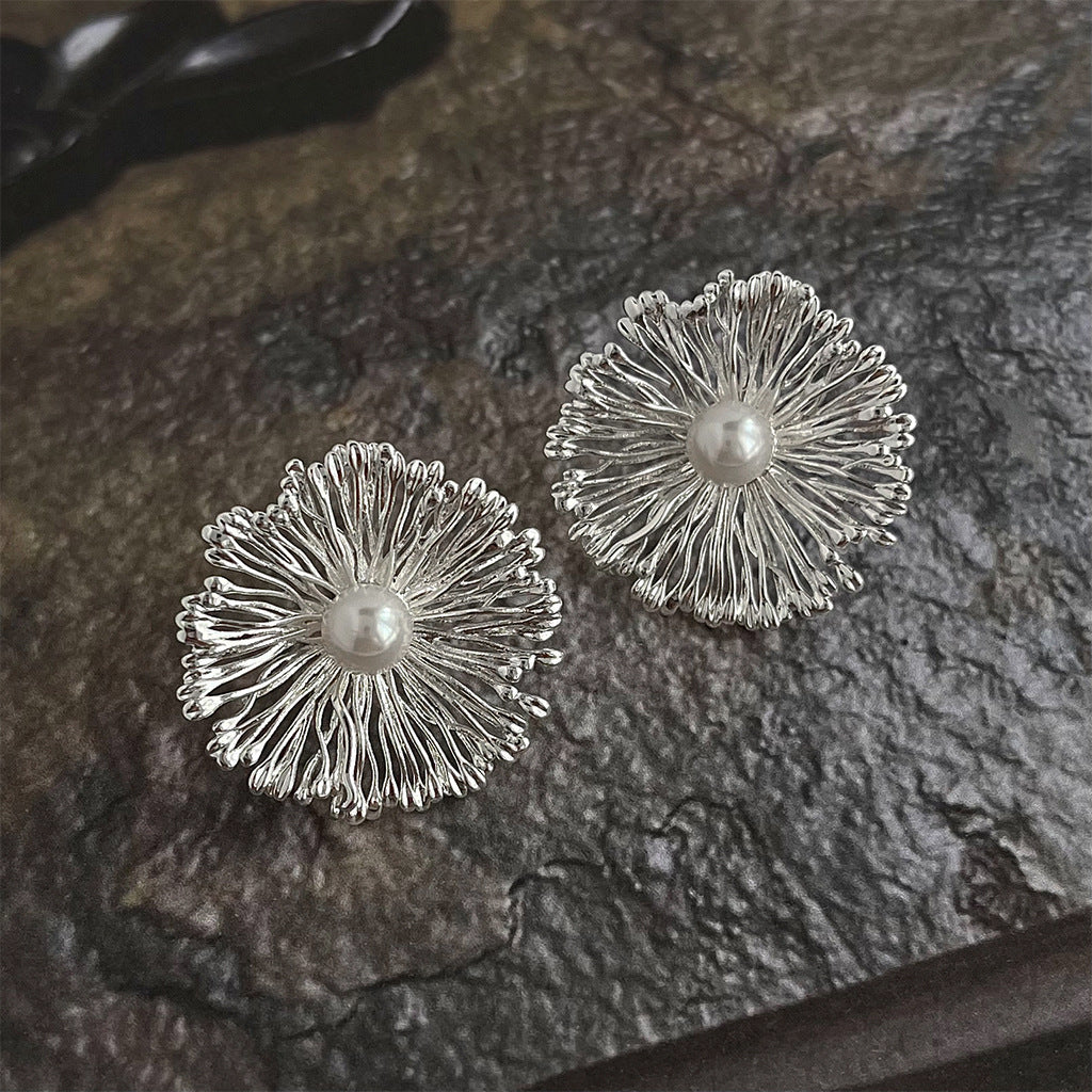 A pair of statement floral earrings crafted from silver-toned brass, each featuring an intricate petal design with a lustrous pearl at the center.