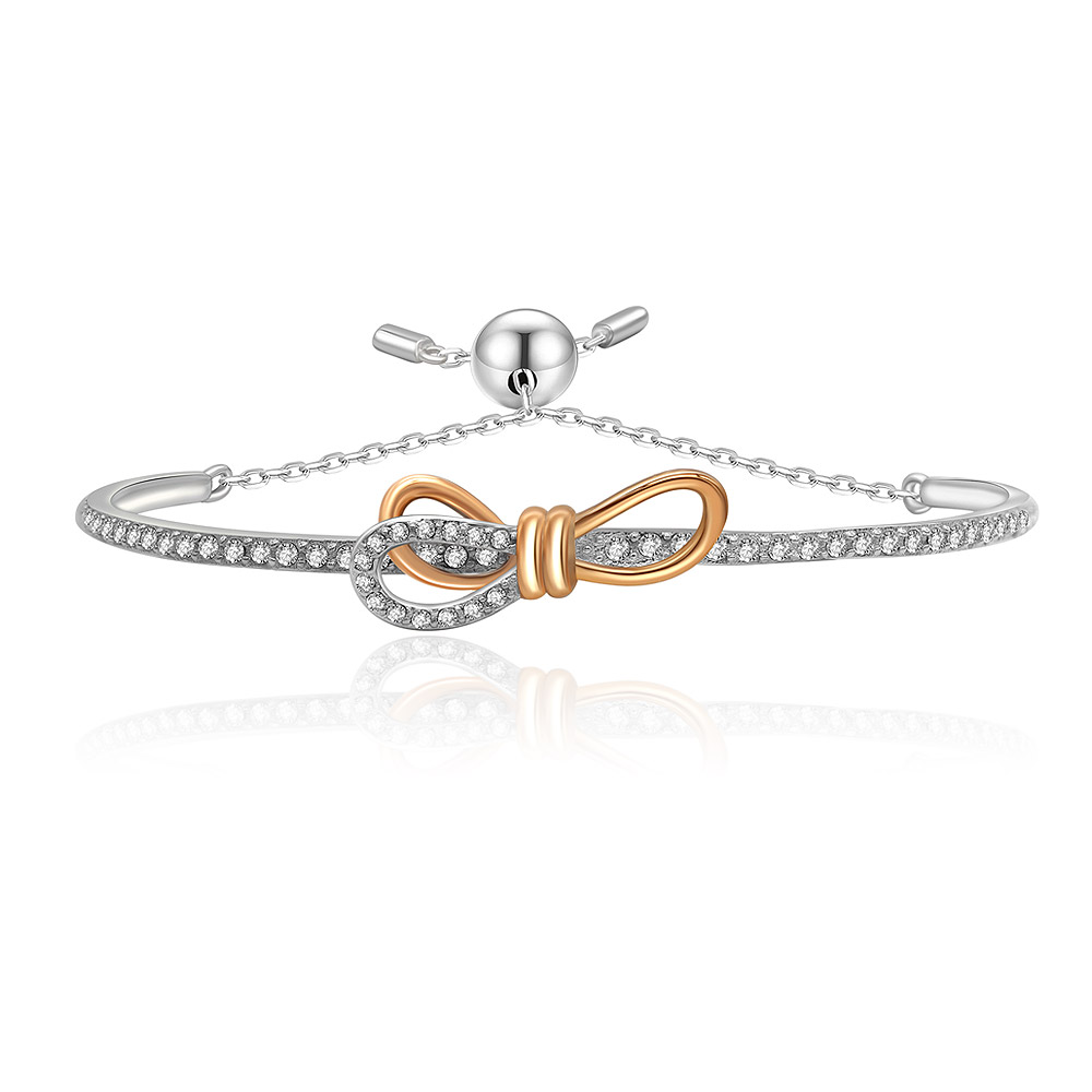 A close-up of the Tied Ribbon Bow Bangle, featuring a two-tone rhodium and rose gold finish with sparkling white cubic zirconia stones.