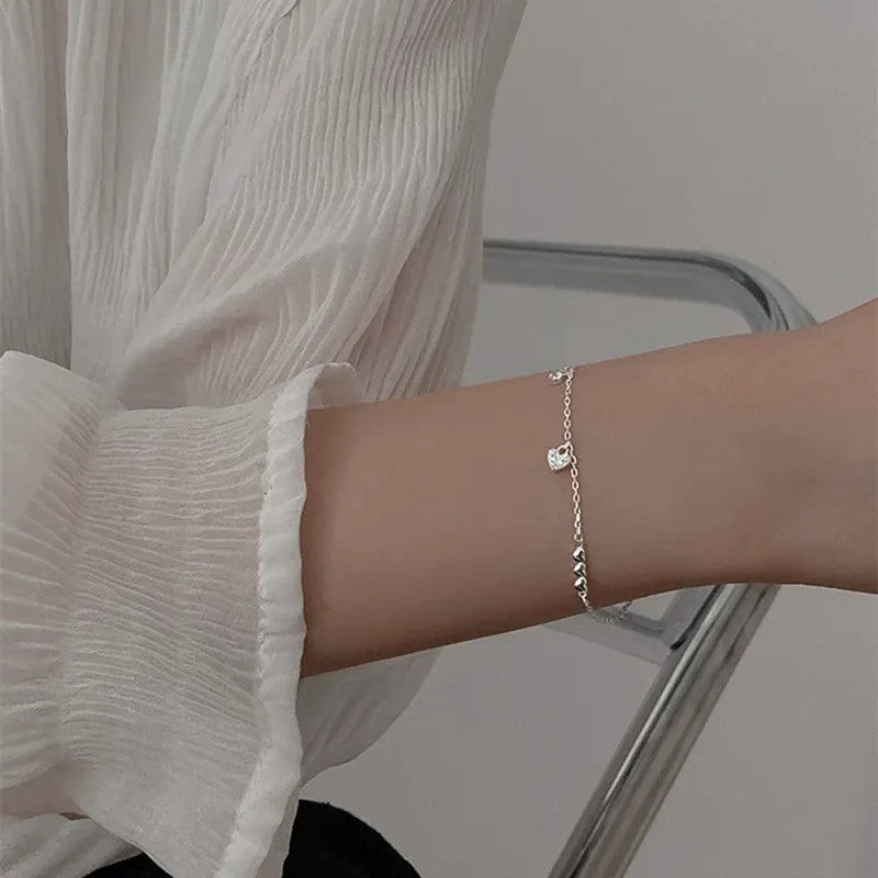 A woman's wrist adorned with the 925 Sterling Silver Connected Hearts Charm Bracelet, highlighting the central heart charm.