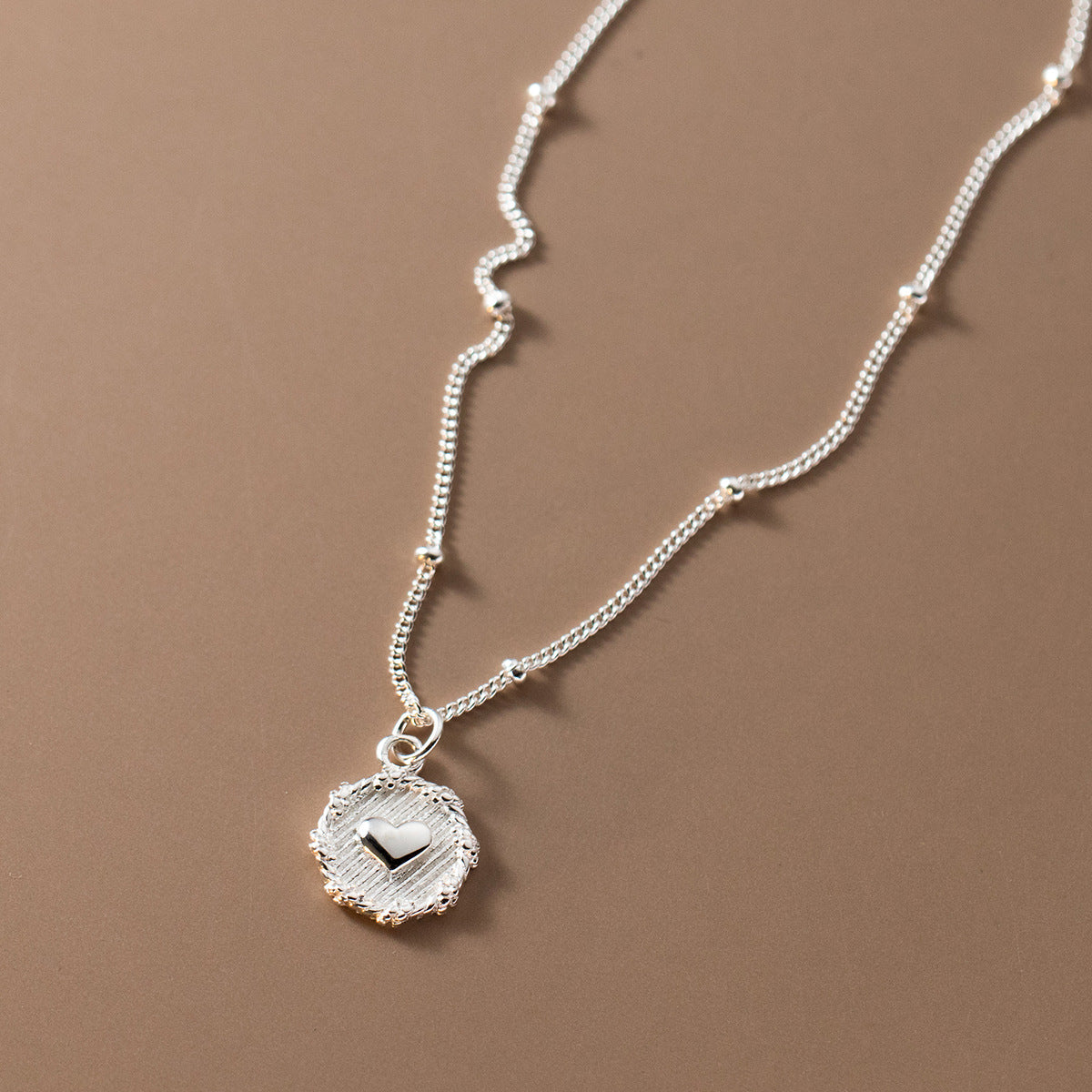 A close-up of a 925 sterling silver necklace featuring a polished heart-shaped pendant on a delicate beaded chain, set against a clean white background.