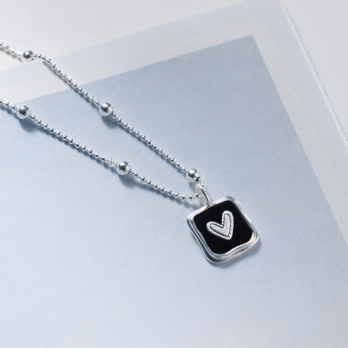 Close-up of a wholesale 925 sterling silver necklace with a simple black square pendant featuring a heart design, on a bead chain.