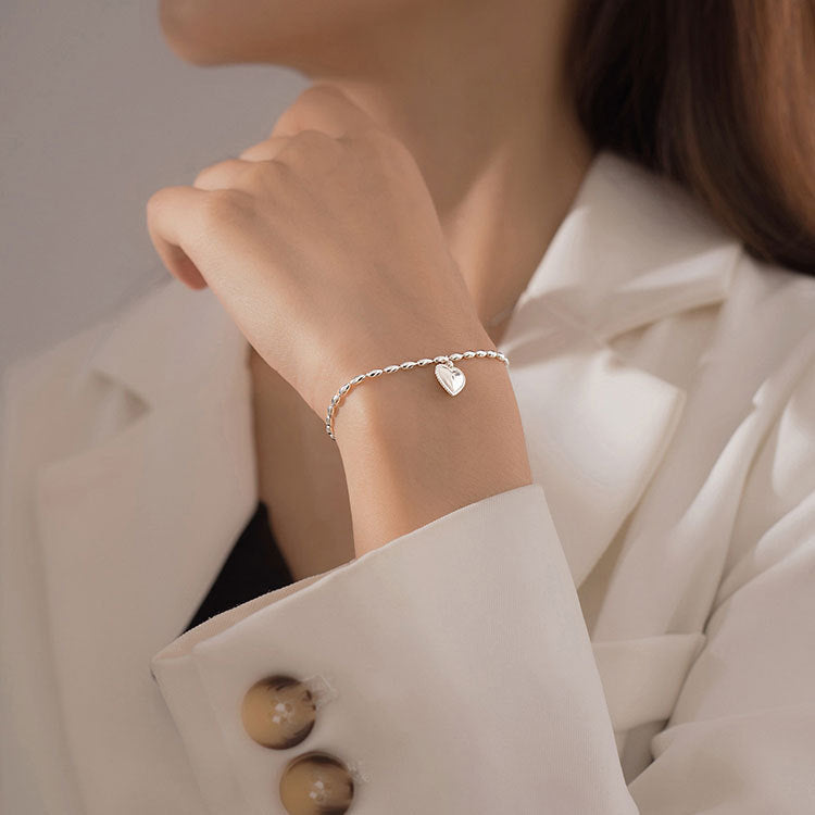A close-up of a woman's wrist wearing an elegant 925 sterling silver rice-beaded chain bracelet with a polished heart pendant.