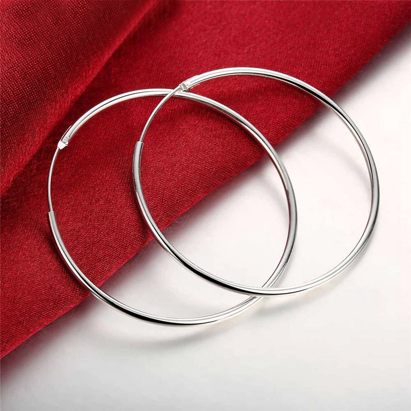 A pair of classic 50mm 925 sterling silver hoop earrings displayed on a rich red fabric background.