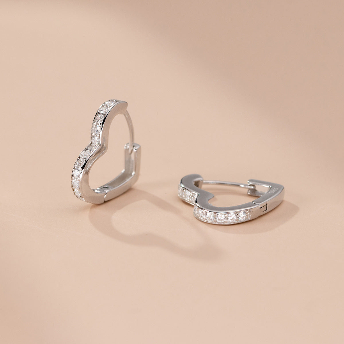 A pair of 925 sterling silver heart hoop earrings, elegantly accented with sparkling cubic zirconia stones, displayed on a white background.