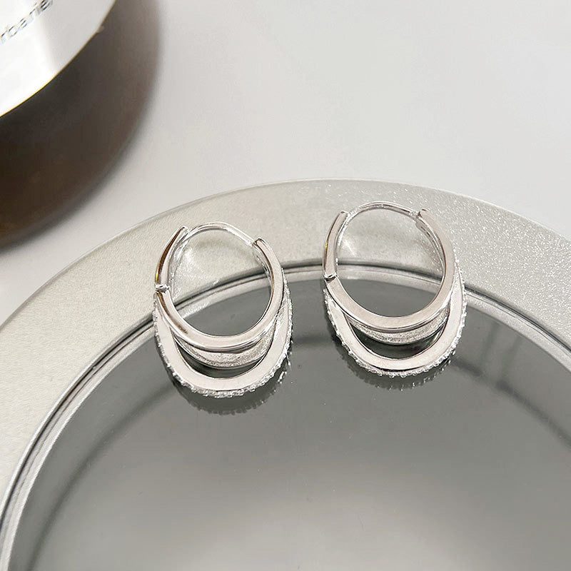 A detailed close-up of 925 sterling silver hoop earrings featuring a unique triple-layered design with sparkling CZ stones, showcasing fine craftsmanship.