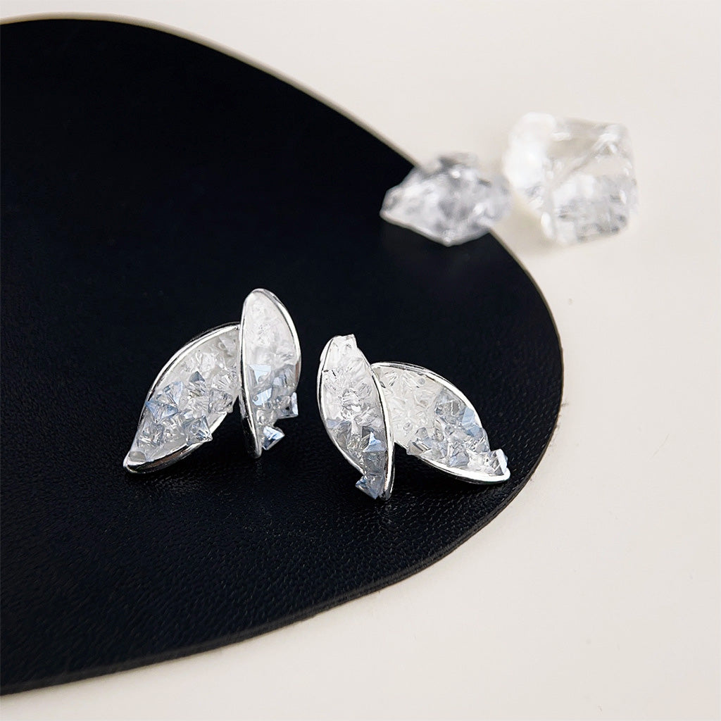 A pair of silver-plated leaf-shaped stud earrings with clear crystal glass, displayed on a black stand.