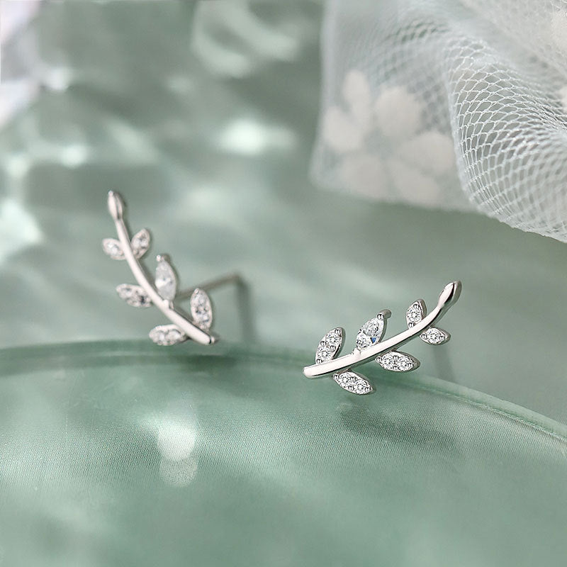 A pair of 925 sterling silver olive leaf stud earrings with sparkling CZ zircon stones, elegantly displayed on a green satin background.