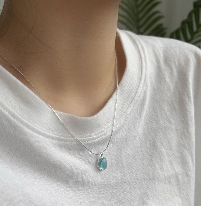 A model wearing the 925 Sterling Silver Opal Necklace, showcasing the delicate blue pendant against a white shirt.