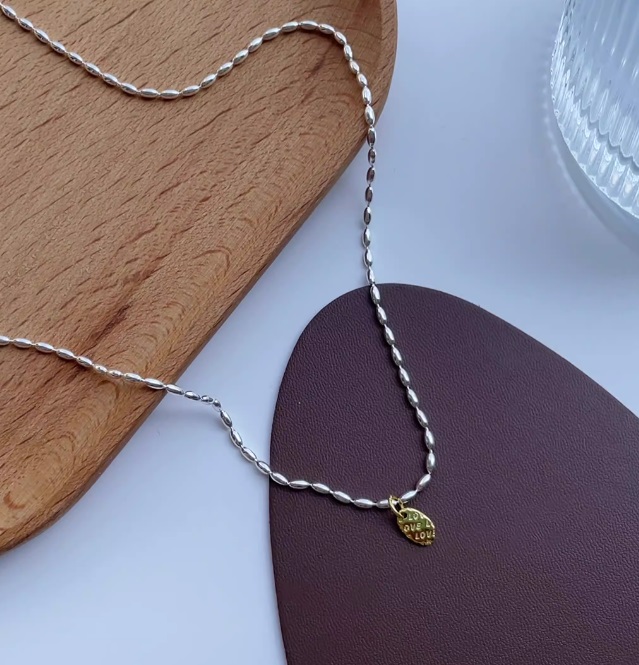 Close-up of a 925 sterling silver bead chain necklace with a gold pendant engraved with the words 'BE' and 'LOVE'.