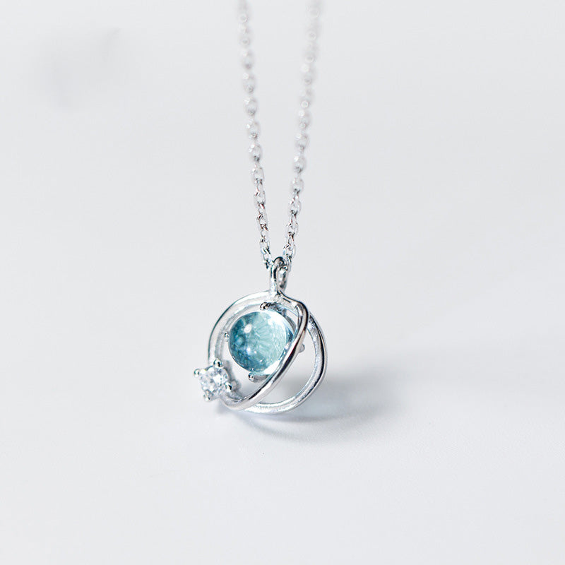 A close-up of a 925 sterling silver planet pendant necklace, featuring a light blue gemstone centerpiece and a smaller clear stone accent, from the set of 5 collection.