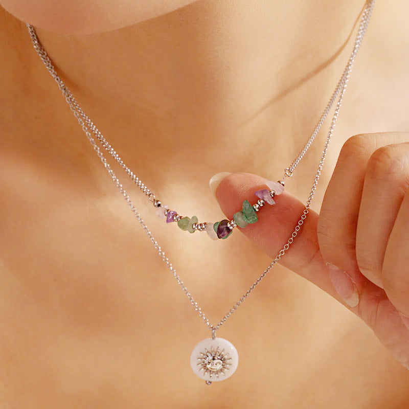 A set of two stainless steel layered necklaces, one with colorful rock beads and the other with a delicate sun pendant, displayed on a neutral background.