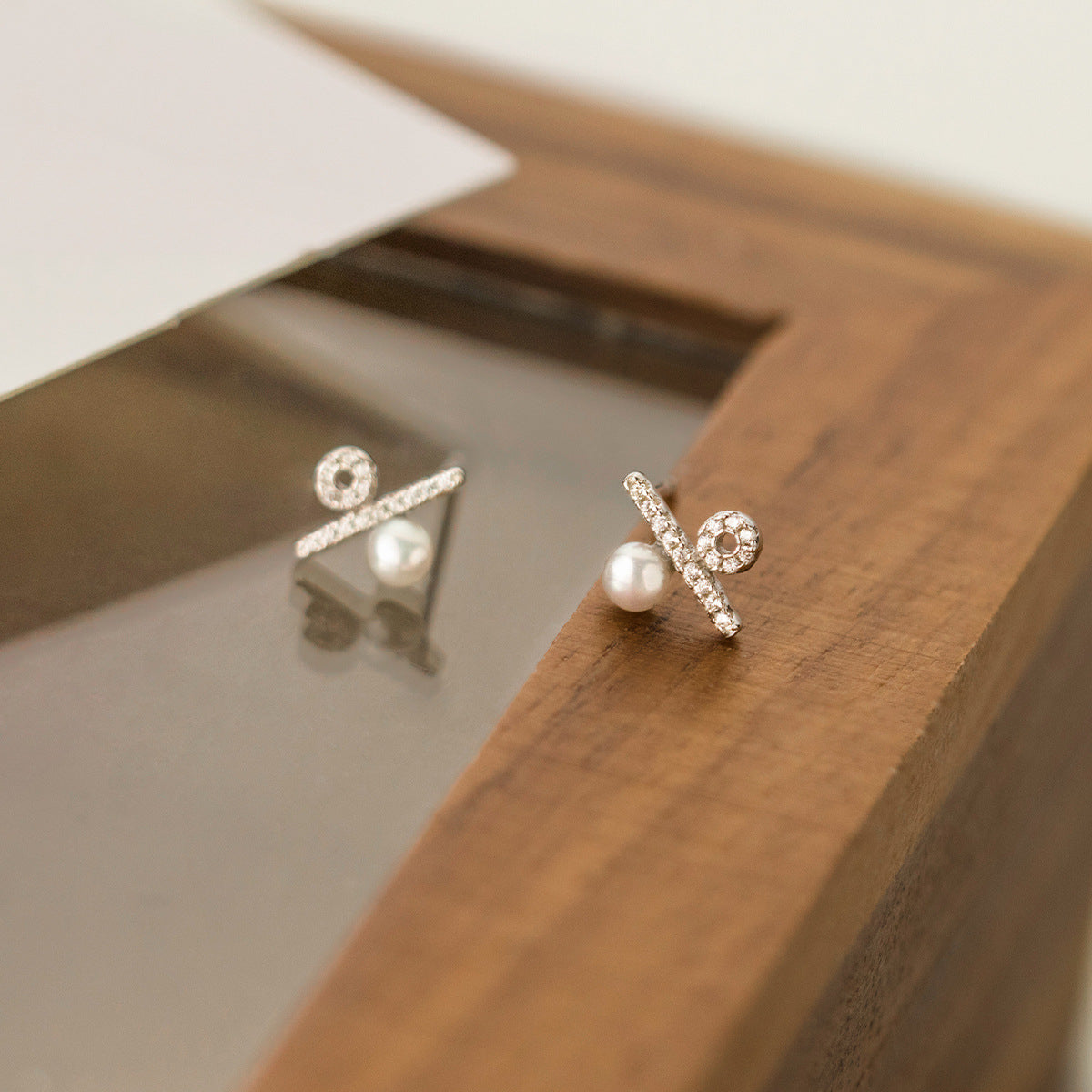 A pair of Silver 925 stud earrings featuring a delicate pearl and a crisscross design adorned with sparkling CZ stones, on a clean white background.