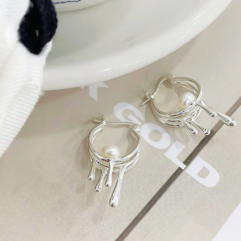 A studio product shot of 925 sterling silver pearl drop liquid hoop earrings, showcasing their unique flowing design and central pearl accent against a clean background.