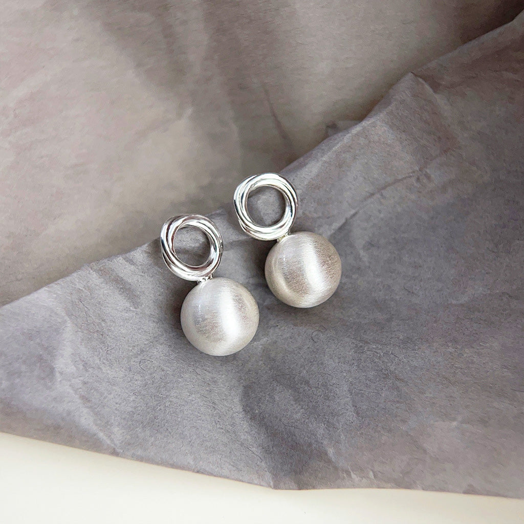 A pair of fashion-forward matte silver 3D ball stud earrings with a simple, elegant design, shown against a white background.