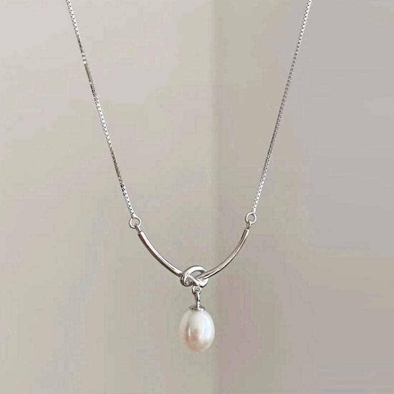 A close-up of an elegant silver-plated knot-drop pearl pendant necklace, displayed on a neutral background.