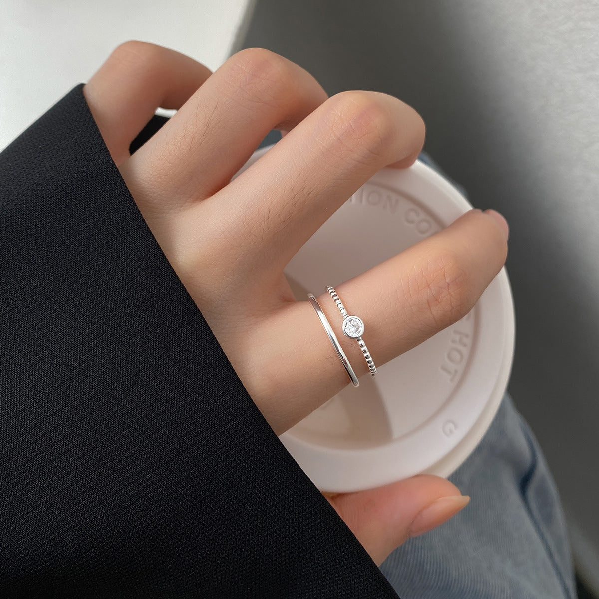 A woman's hand wearing the 925 Sterling Silver Round Zircon Adjustable Rings, showcasing their elegant double-layer design while holding a cup of coffee.