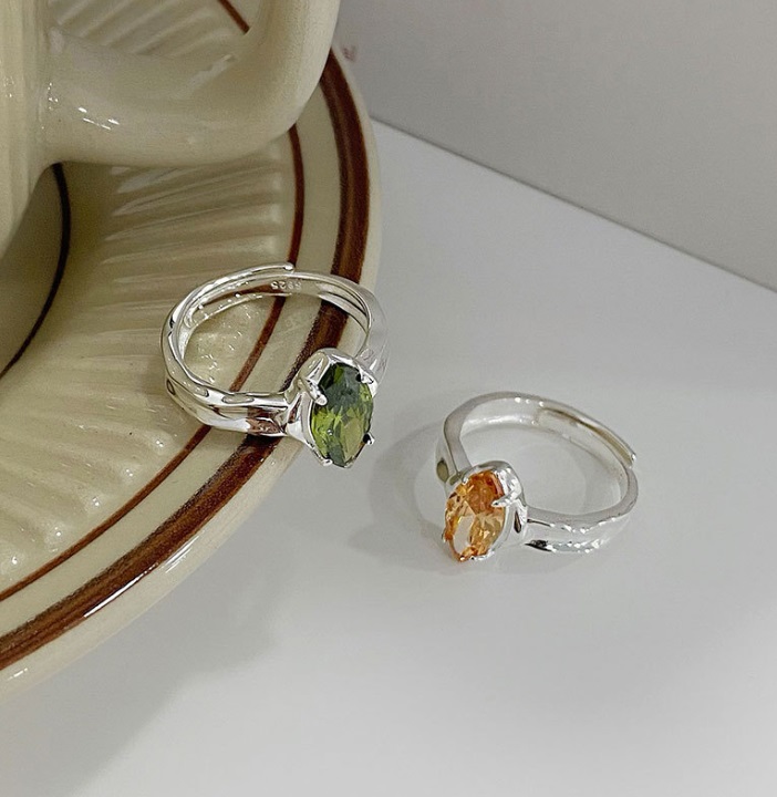 A pair of 925 sterling silver rings, one with a vibrant green peridot gemstone and the other with a warm champagne-colored gemstone, showcasing the adjustable band design.