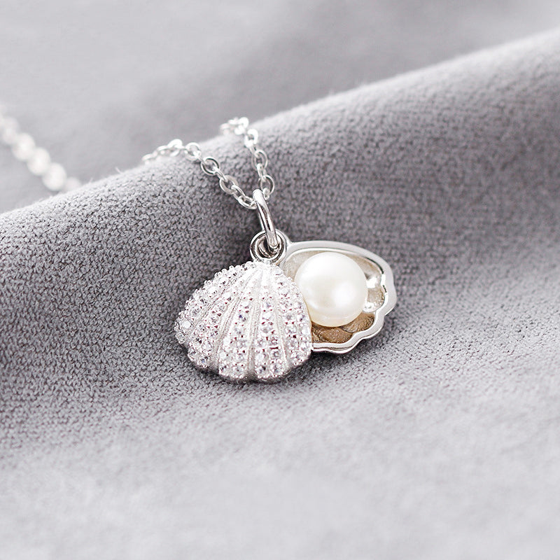 Close-up of a 925 sterling silver seashell pendant, revealing a delicate pearl nestled inside. The pendant has a polished, high-shine finish.