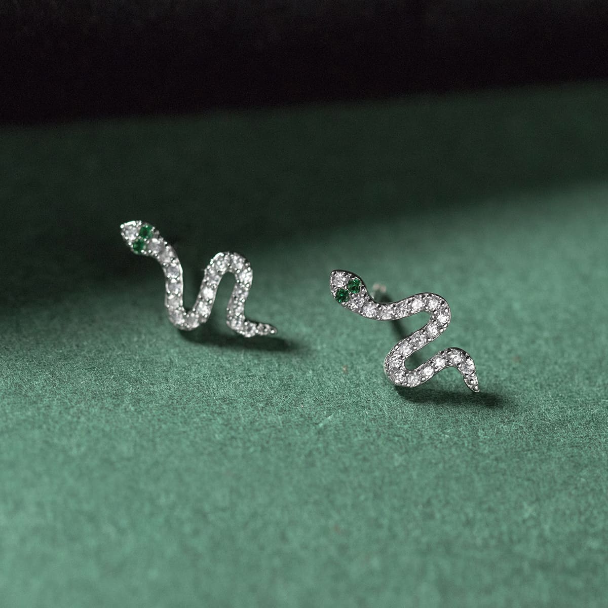 A pair of hypoallergenic 925 sterling silver snake stud earrings with clear and green CZ gemstone accents, designed for sensitive ears.