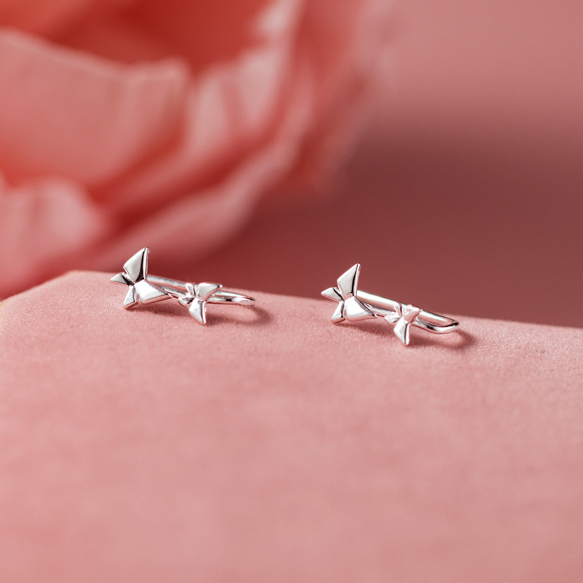 A pair of creatively designed sterling silver star-shaped hook earrings from the 5-pair set, displayed on a soft pink background.