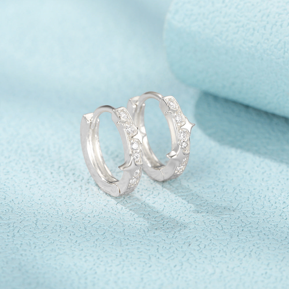 A pair of 925 sterling silver star-shaped hoop huggie earrings, featuring sparkling zircon CZ stones, displayed on a light blue background.