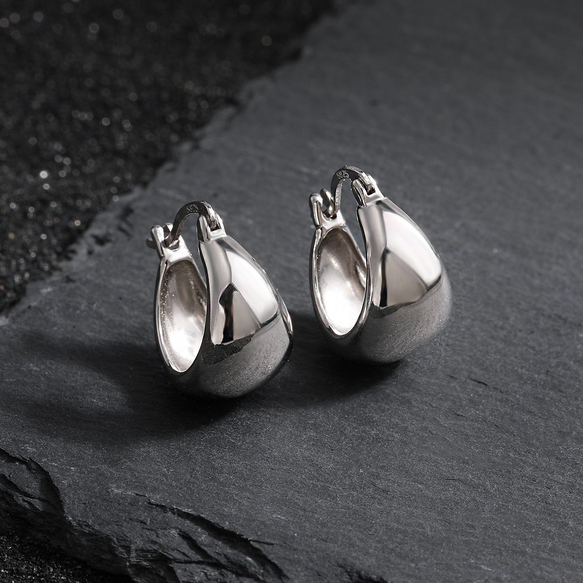 A pair of wholesale 925 sterling silver chunky hoop earrings with a white gold plated finish, showcasing their minimalist teardrop-like shape and secure clasp.