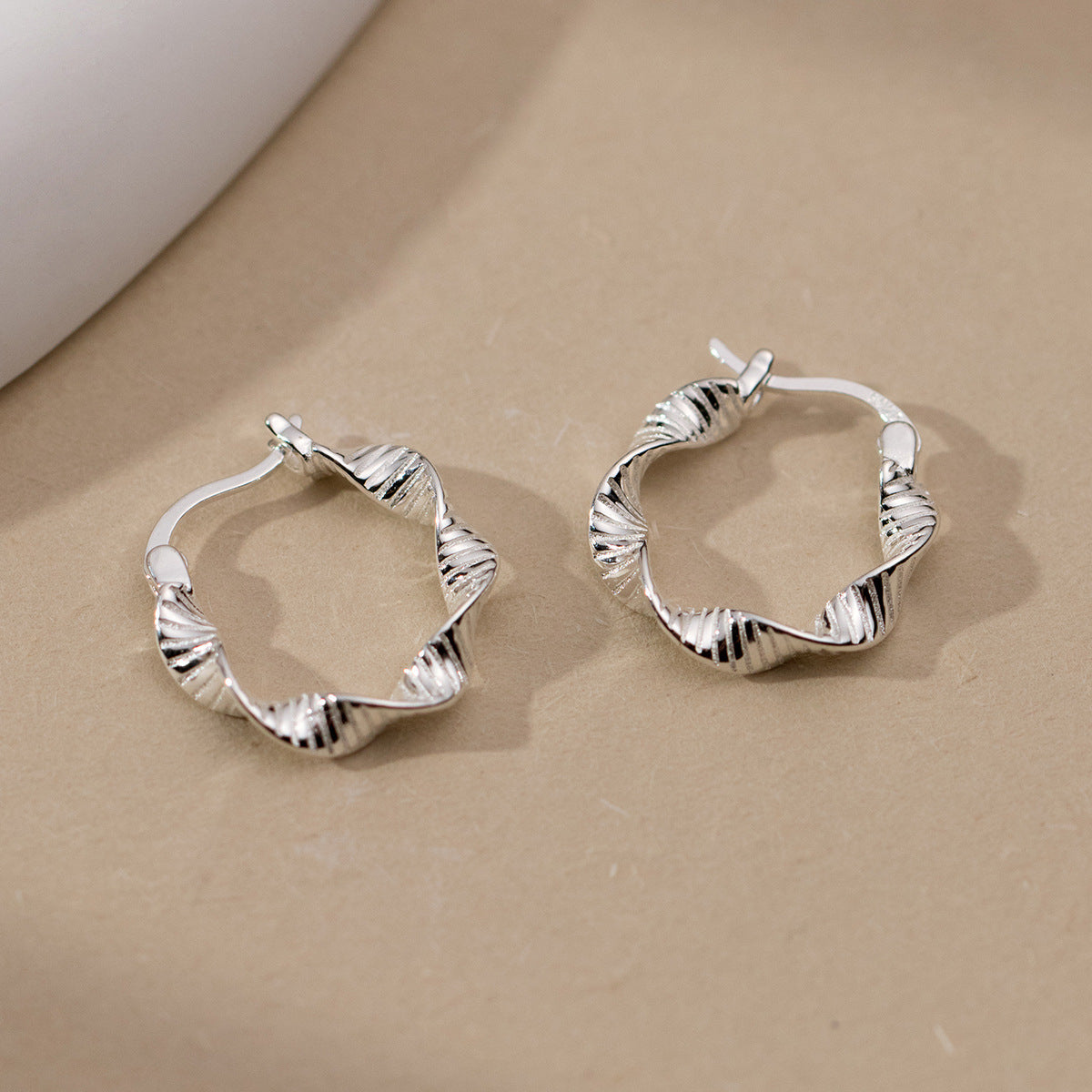 A pair of 925 sterling silver hoop earrings with an elegant twisted geometric design, showcased on a neutral background.