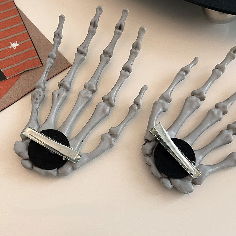 A pair of gray plastic skeleton hand hair clips with silver metal clips, shown on a plain background. Ideal for punk fashion and Halloween costumes.
