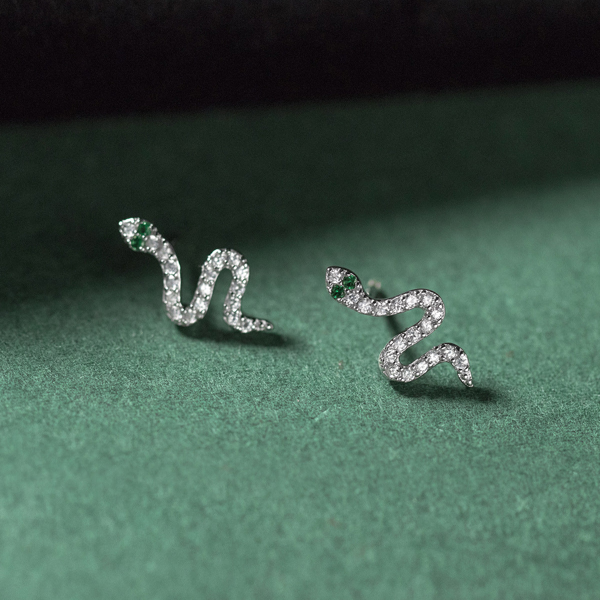 A pair of 925 sterling silver snake design stud earrings, intricately detailed with sparkling clear and green gemstones.