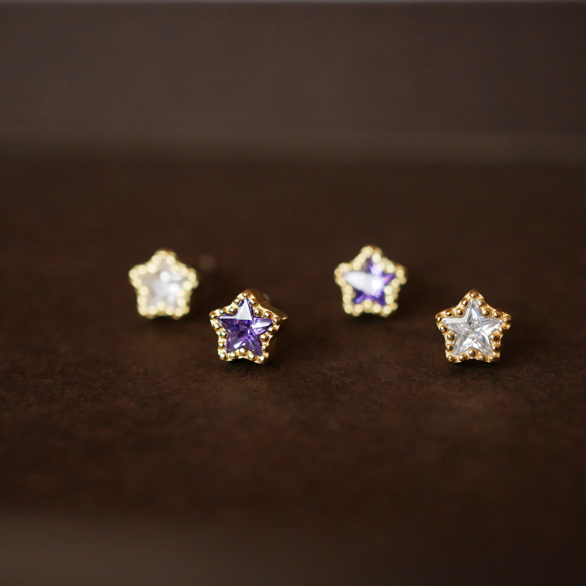 A promotional shot of four 925 sterling silver five-pointed star stud earrings, plated in gold and set with sparkling gemstones.