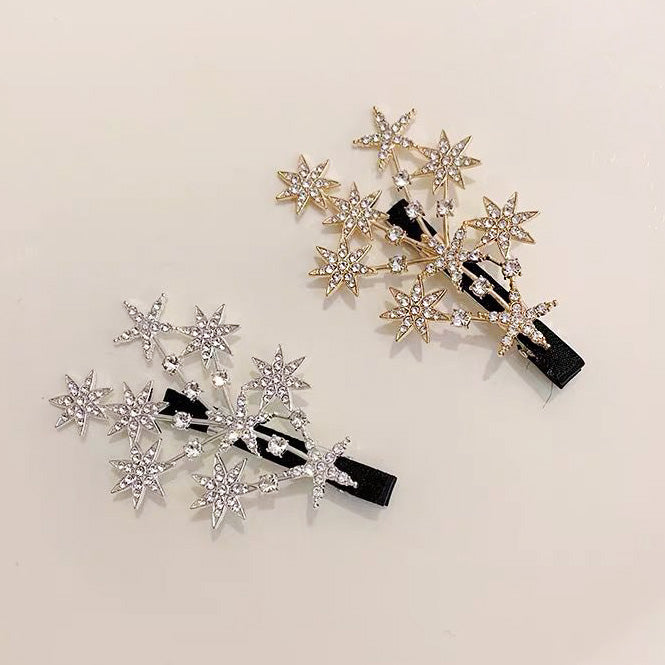 A pair of sparkly crystal star hair clips, one in a polished gold finish and the other in a brilliant silver finish, displayed side-by-side.