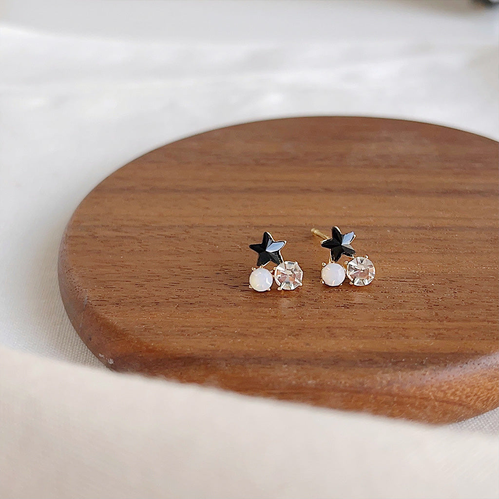A set of gold-plated stud earrings featuring black star designs with sparkling zircon, pearl, and crystal accents, presented on a white background.