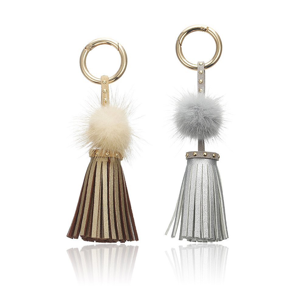 A pair of leather with faux fur tassel keychains, style JRK-005, one with gold hardware and a light tassel, the other with silver hardware and a dark tassel.