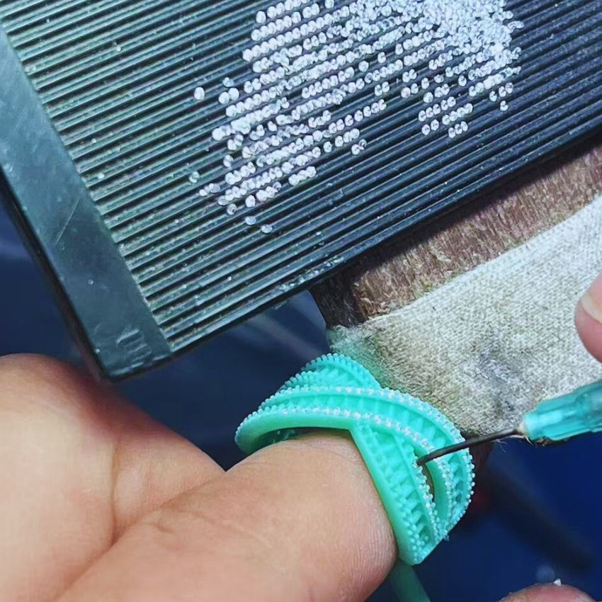 En skicklig hantverkare på JR Fashion Accessories som använder ett precisionsverktyg för steninställning, noggrant applicerande ädelstenar på ett skräddarsytt smycke.