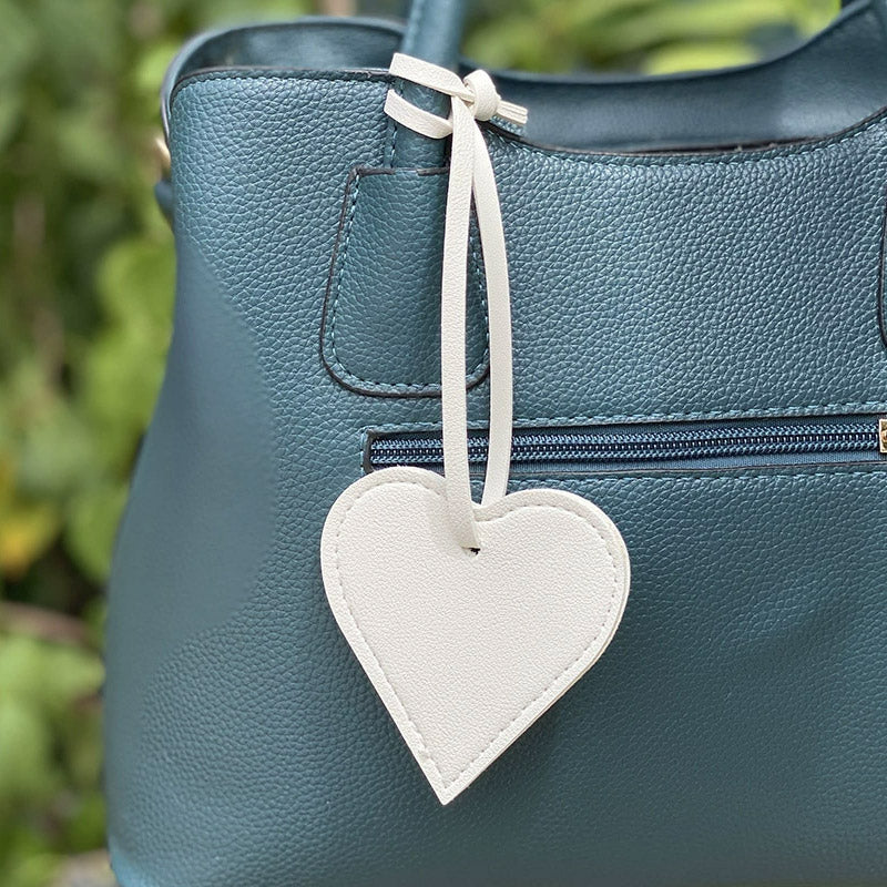 A stylish teal leather handbag adorned with a chic, flat white PU leather heart-shaped bag charm, showcasing its use as a fashion accessory.