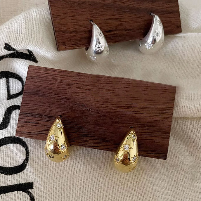 A pair of 925 sterling silver and a pair of gold-plated chunky hoop earrings, both featuring a prominent star design with zircon accents, displayed side-by-side.