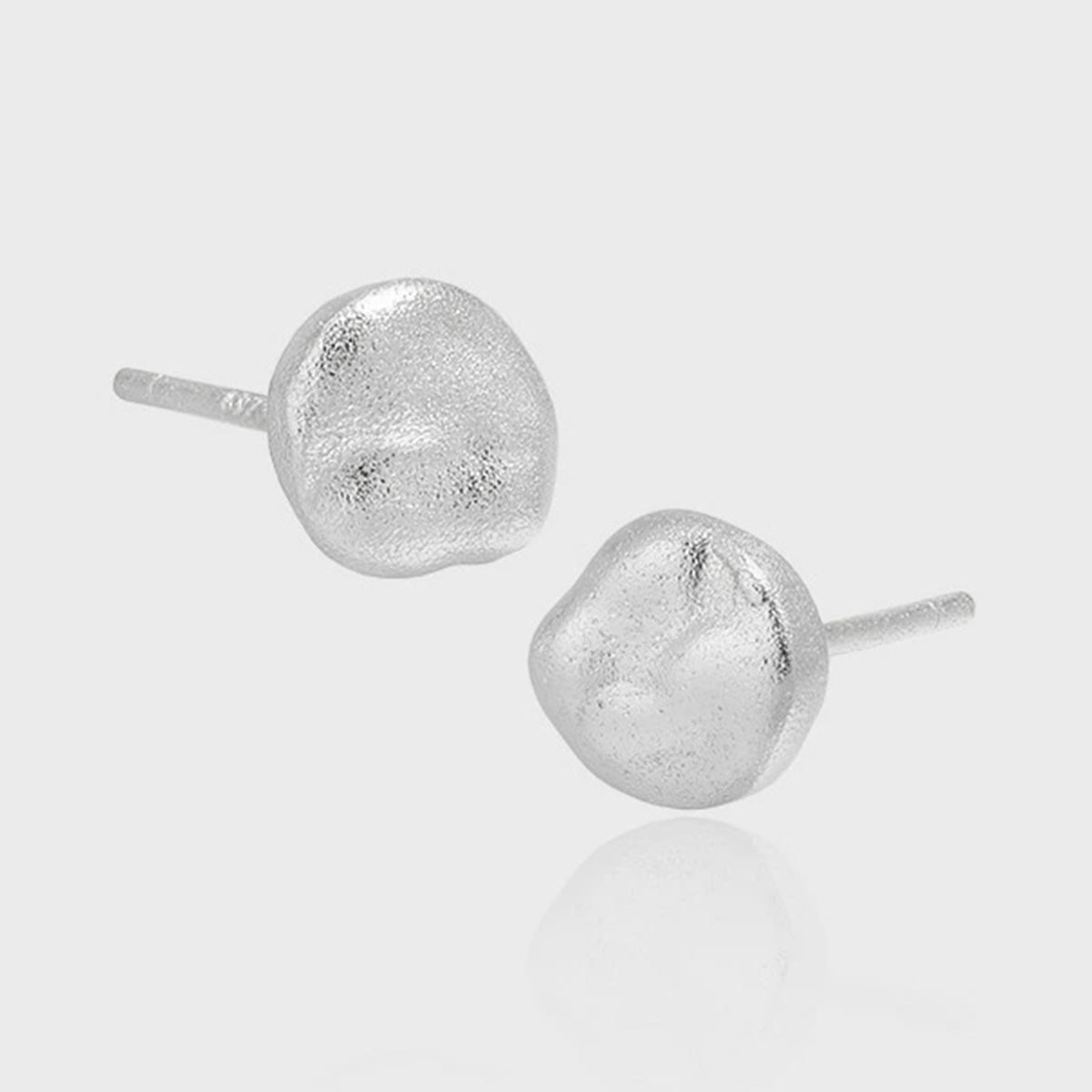 A pair of minimalist 925 sterling silver round stud earrings, one in 18K gold plate and one in silver, displayed on a textured surface to showcase their simple, elegant design.