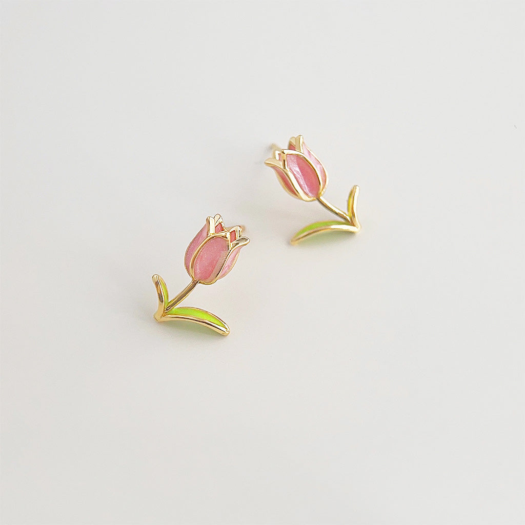 A pair of 14k gold-plated enamel tulip stud earrings with delicate pink petals and green leaves, showcasing the detailed craftsmanship.
