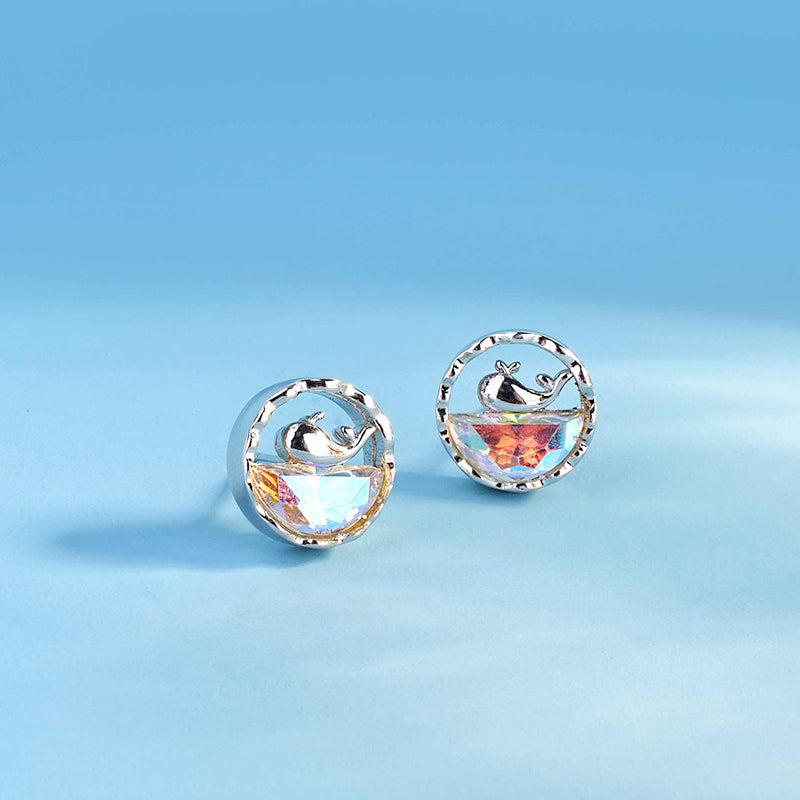 A detailed close-up of the 925 sterling silver whale stud earrings, highlighting the polished silver whale figure resting on a captivating rainbow opal stone.