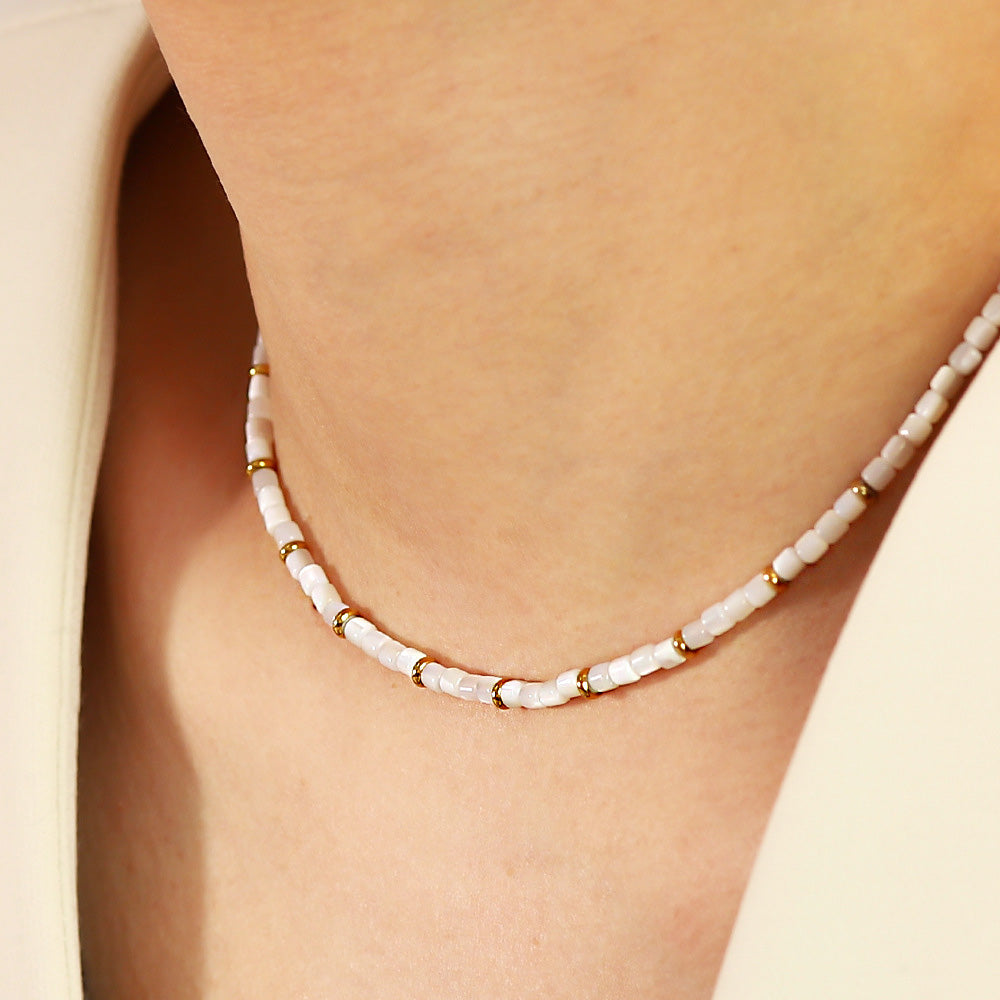 A model showcasing the elegant waterproof stainless steel necklace with white shell beads and a gold-tone finish.