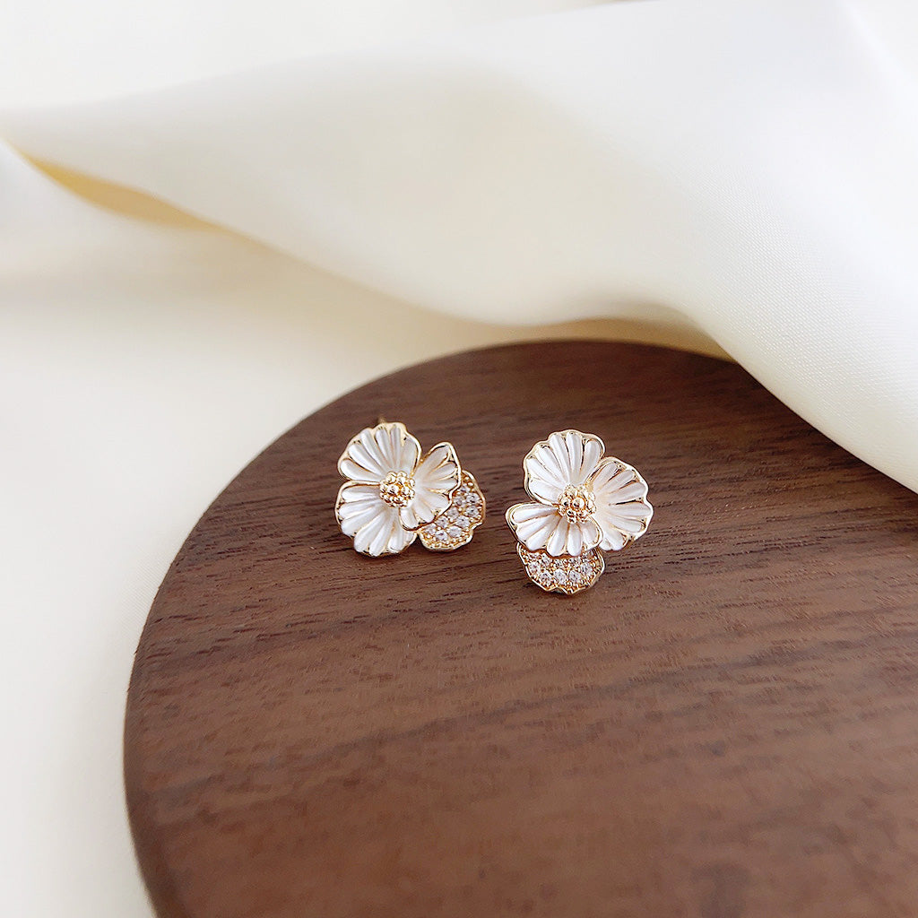 A pair of 14k gold plated flower stud earrings with white enamel petals and a central zircon stone on a white background.