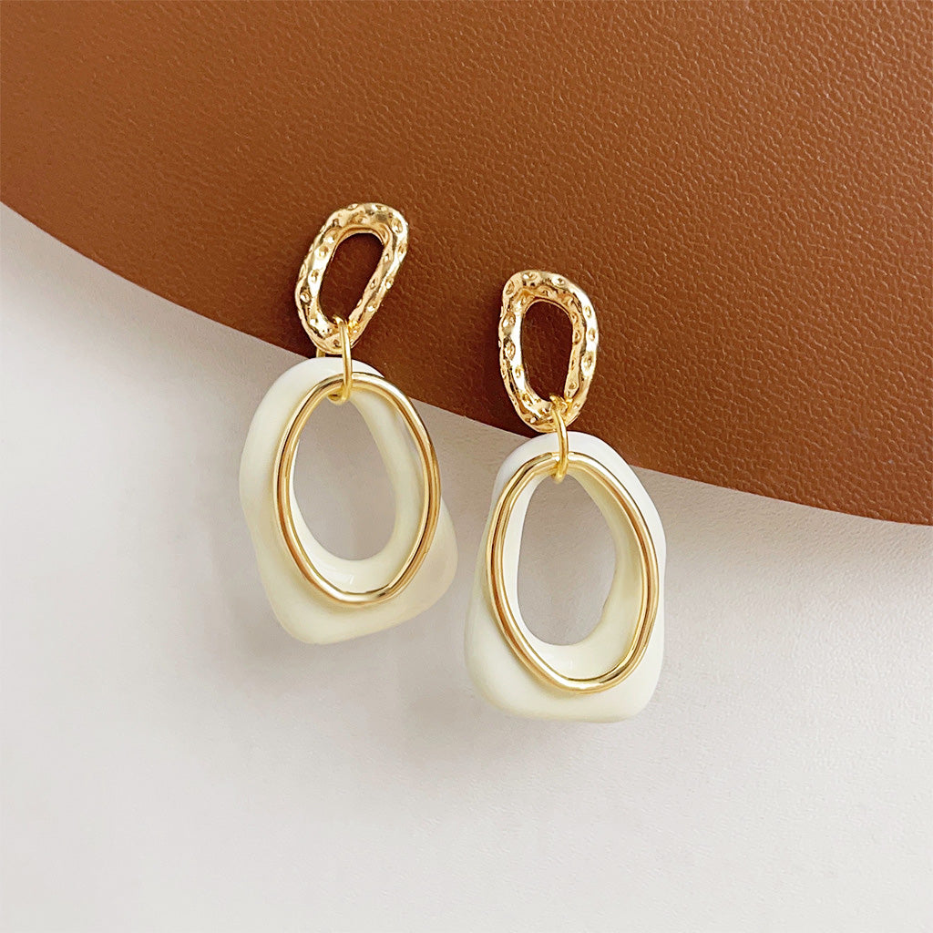 A pair of wholesale geometric overlapping drop earrings featuring a white enamel oval piece and a textured 14K gold-plated top piece, on a clean white background.