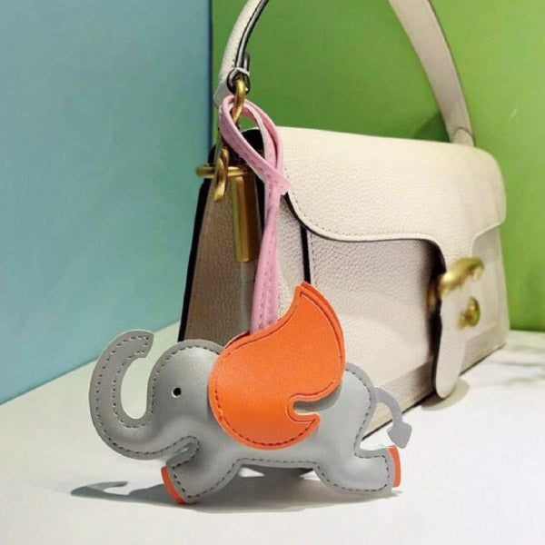 A cute white PU leather elephant bag charm with colorful accents, attached to the strap of a stylish white handbag.